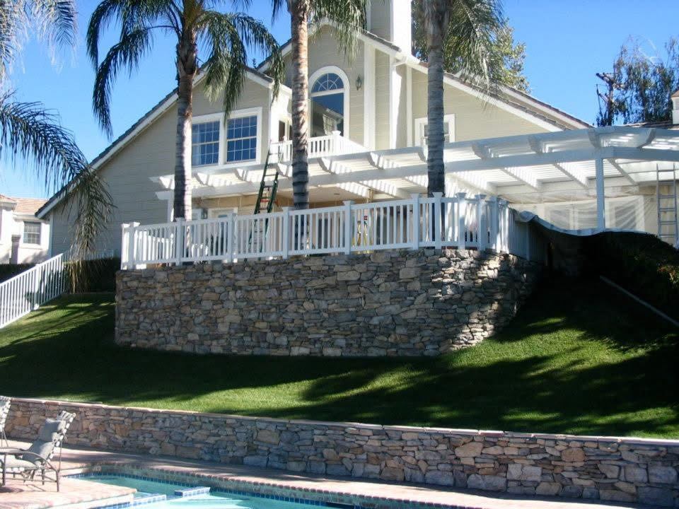 Vinyl railing atop a stacked stone retaining wall by a pool